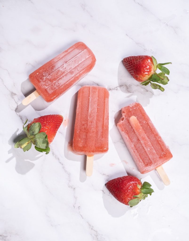 three popsicles with strawberries on a marble surface